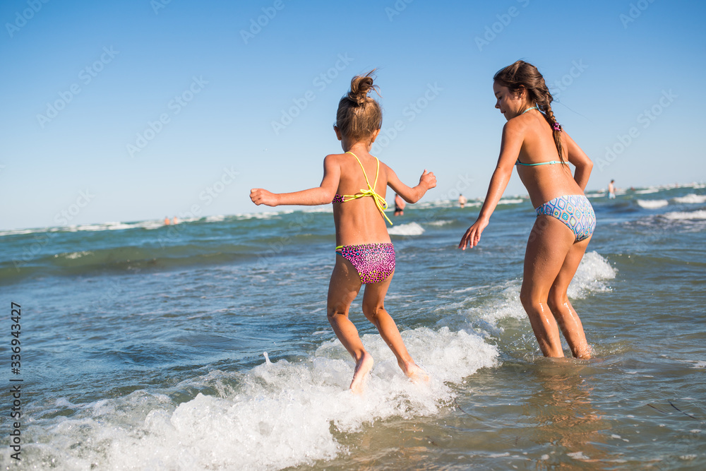 Two funny little girls jump in the noisy sea waves and enjoy the long-awaited vacation on a sunny warm summer day. Concept of sea vacation and travel with children Two funny little girls jump in the noisy sea waves and enjoy the long-awaited vacation on a sunny warm summer day. Concept of sea vacation and travel with children