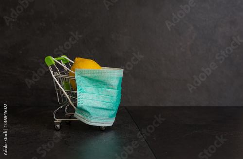 Supermarket cart in the green medical mask, on a black background. Lemon in a cart. Protection against coronavirus.Health and vitamin therapy. Prevention of diseases. © Glebsterr