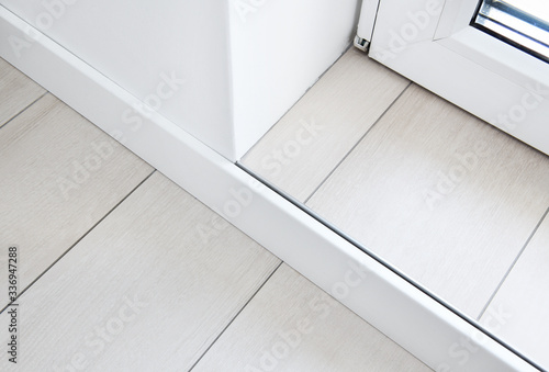 The floor is made of ceramic tiles, granite. Imitation of a wooden board. Connection of a floor with a threshold of a balcony. A white MDF skirting board is adjacent to the threshold.