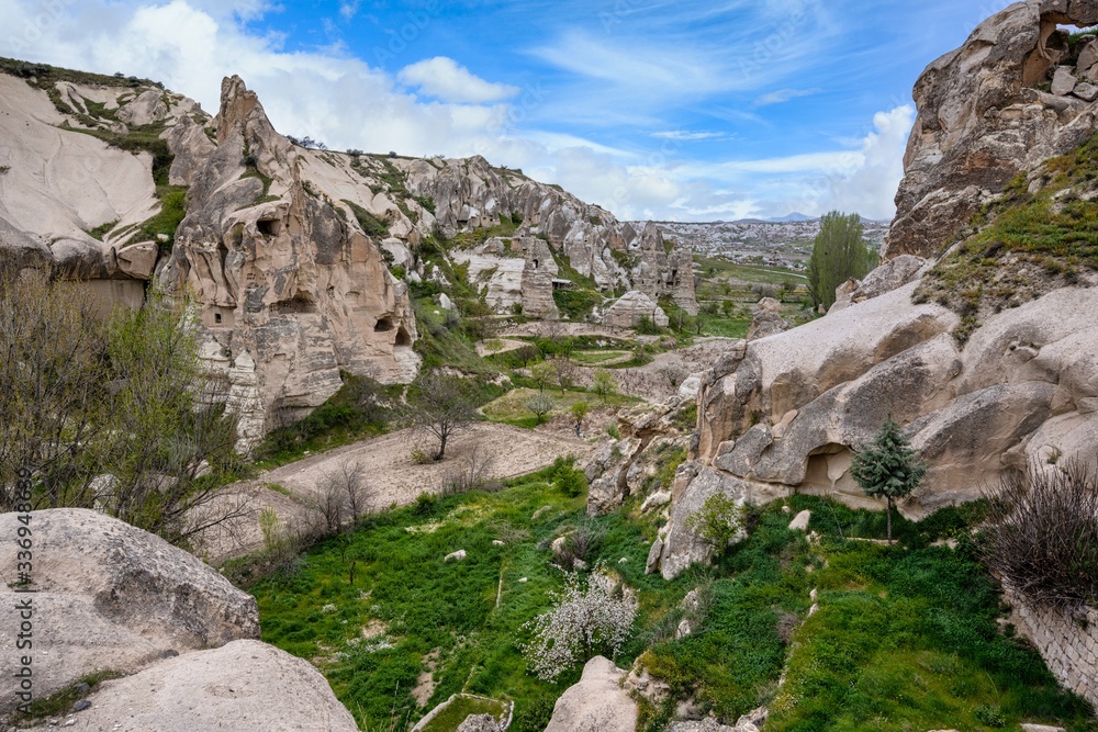 The Zelve Open Air Museum in Cappadocia, Turkey, has many sharp limestone mountains in the summer. There are green grass all over the area with blue skies.