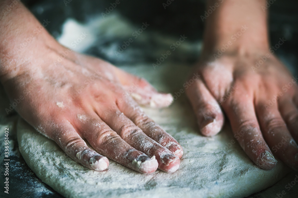 A person prepares pizza dough at home in the kitchen on a baking sheet, rolling it out with his bare hands. A person prepares pizza dough at home in the kitchen on a baking sheet, rolling it out with his bare hands.
