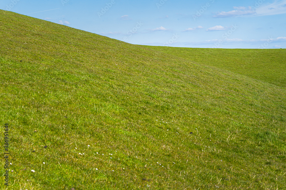 Green grass against blue sky with white clouds, Netherlands dike landscape along the Dutch coast Green grass against blue sky with white clouds, Netherlands dike landscape along the Dutch coast