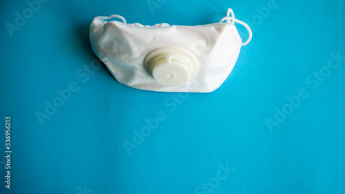 White protective medical mask with a valve on a blue background with copy space. Protective face mask against pollution, viruses, flu and coronavirus. Health care and surgical concept.