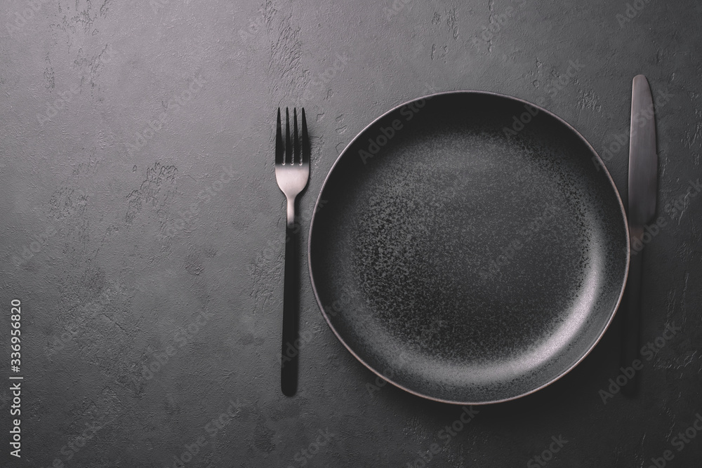 Empty black ceramic plate and cutlery on a stone dark table. Dark background for menu or recipe Empty black ceramic plate and cutlery on a stone dark table. Dark background for menu or recipe