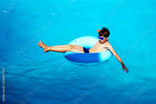 Beautiful young boy with inflatable ring relaxing in blue swimming pool
