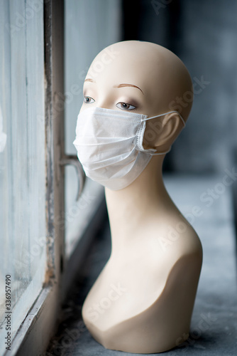 manikin girl with COVID-19 2019-NCOV looks out the window in a medical mask