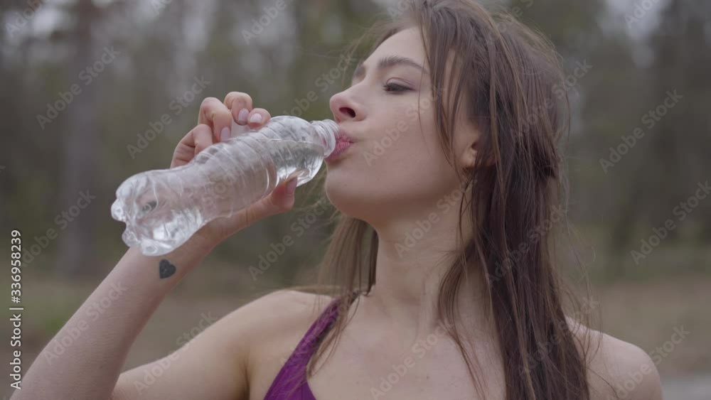 Close-up of young gorgeous sportswoman drinking water in park and leaving. Portrait of confident brunette girl training outdoors in the morning. Hobby, lifestyle, sport, fitness. Close-up of young gorgeous sportswoman drinking water in park and leaving. Portrait of confident brunette girl training outdoors in the morning. Hobby, lifestyle, sport, fitness.