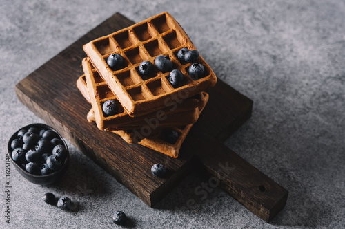 Belgian waffles with blueberries on cutting board. Traditional breakfast pastries