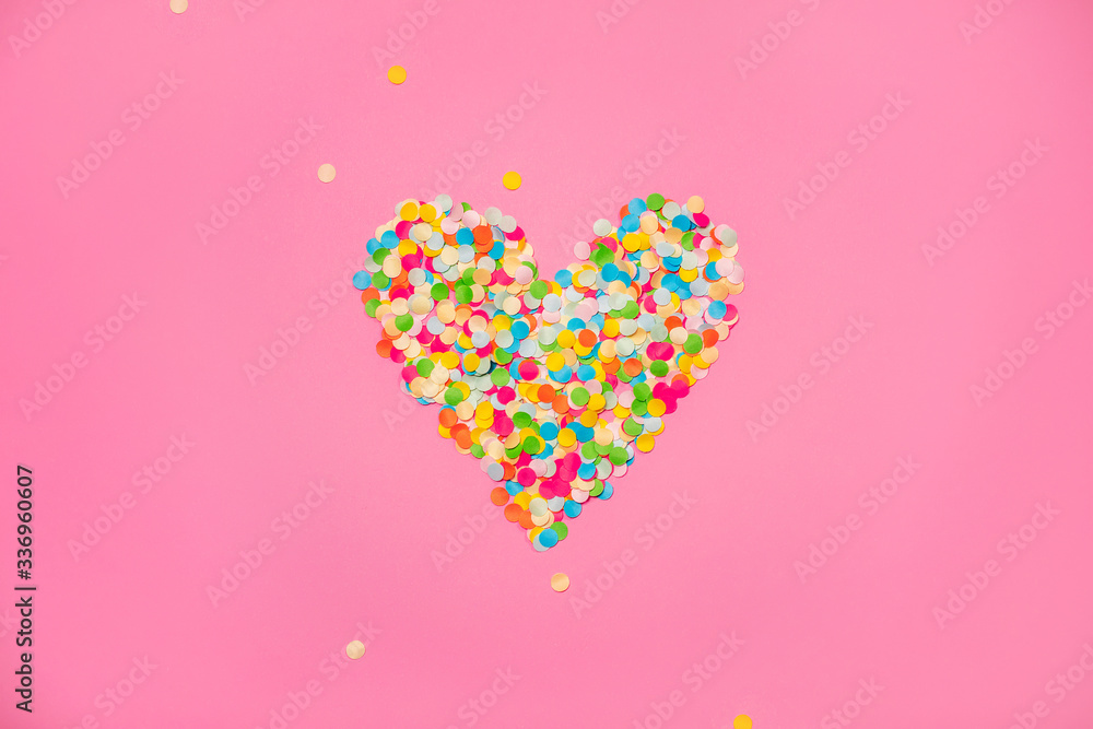 Heart shape made of colorful confetti. Pink backdrop with scattered paper circles. Beautiful decor for the party. Festive backgrond for love story. Valentine's day symbol. View from above. Flat lay.