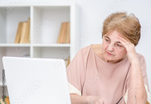 Sad elderly woman looks at laptop in the office