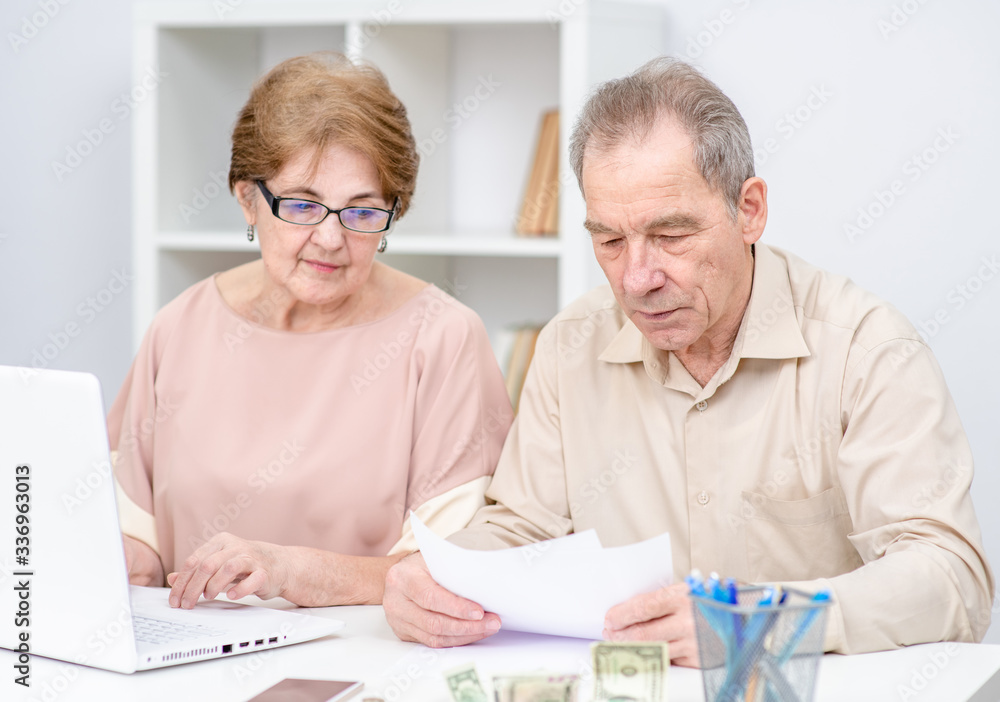 Serious elderly couple calculating bills to pay or doing the income tax declaration online Serious elderly couple calculating bills to pay or doing the income tax declaration online