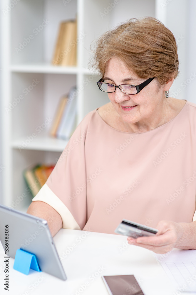 Senior woman holds credit card and use tablet computer. Online shopping Senior woman holds credit card and use tablet computer. Online shopping
