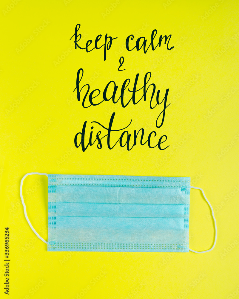 Social distancing. Medical mask on yellow background with lettering. Stop Covid-19. The world pandemic of coronavirus disease. Keep calm and healthy distance. Surgical mask flat lay. Social distancing. Medical mask on yellow background with lettering. Stop Covid-19. The world pandemic of coronavirus disease. Keep calm and healthy distance. Surgical mask flat lay.