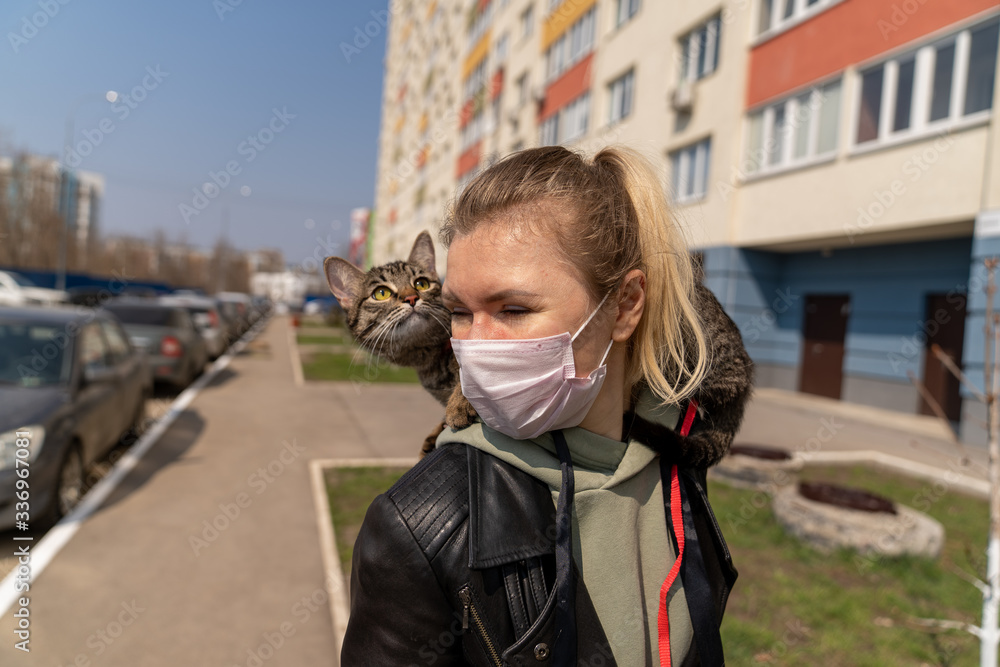 Obraz premium a girl in a medical mask is walking with a kitten on her shoulder