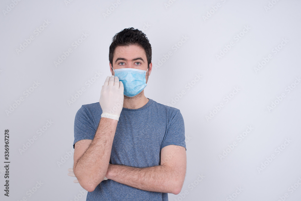 Isolated portrait of stylish European man wearing medical mask with hand near face and looking to the camera with doubtful and skeptical expression suspect and doubt. Isolated portrait of stylish European man wearing medical mask with hand near face and looking to the camera with doubtful and skeptical expression suspect and doubt.