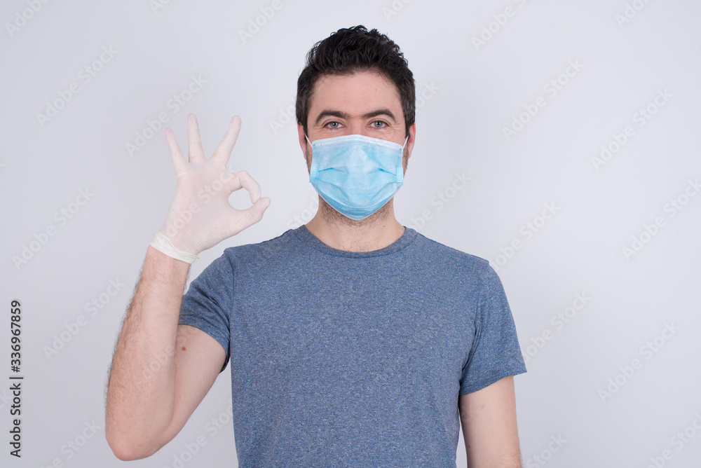 Glad attractive man shows ok sign with hand as expresses approval, has cheerful expression. Photo of handsome male has appealing appearance, being optimistic. Standing against gray wall. Glad attractive man shows ok sign with hand as expresses approval, has cheerful expression. Photo of handsome male has appealing appearance, being optimistic. Standing against gray wall.