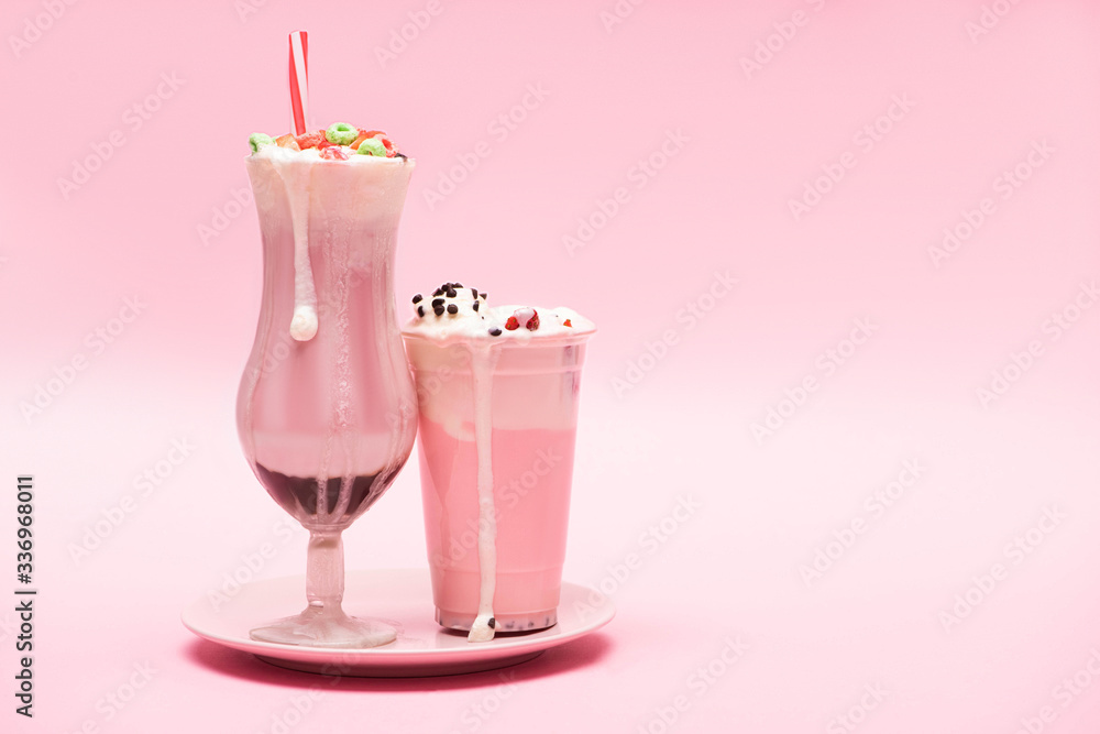 Disposable cup and glass of strawberry milkshakes on plate on pink background Disposable cup and glass of strawberry milkshakes on plate on pink background