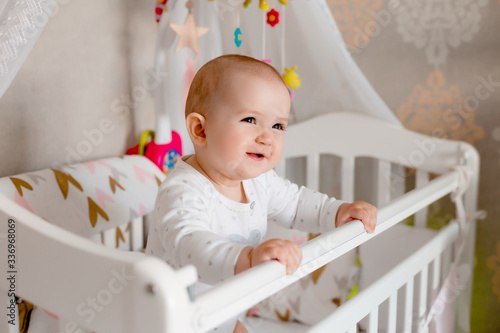 Cute baby girl 8 months sits in baby bed at home