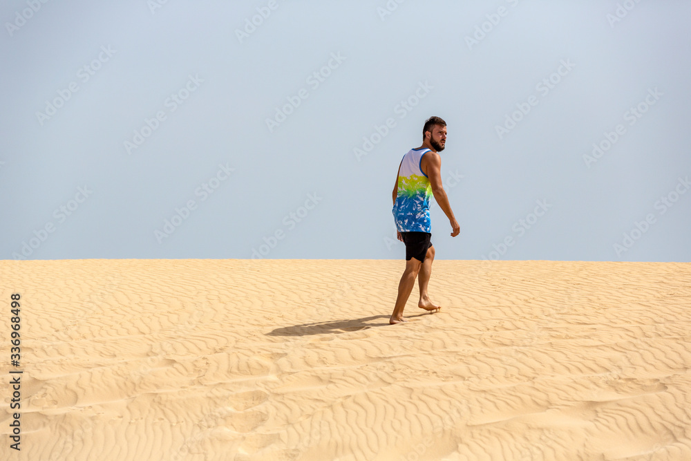 A young handsome man walking on the sand of the dunes in a beach of Fuerteventura