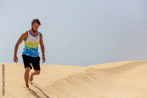 A young handsome man walking on the sand of the dunes in a beach of Fuerteventura