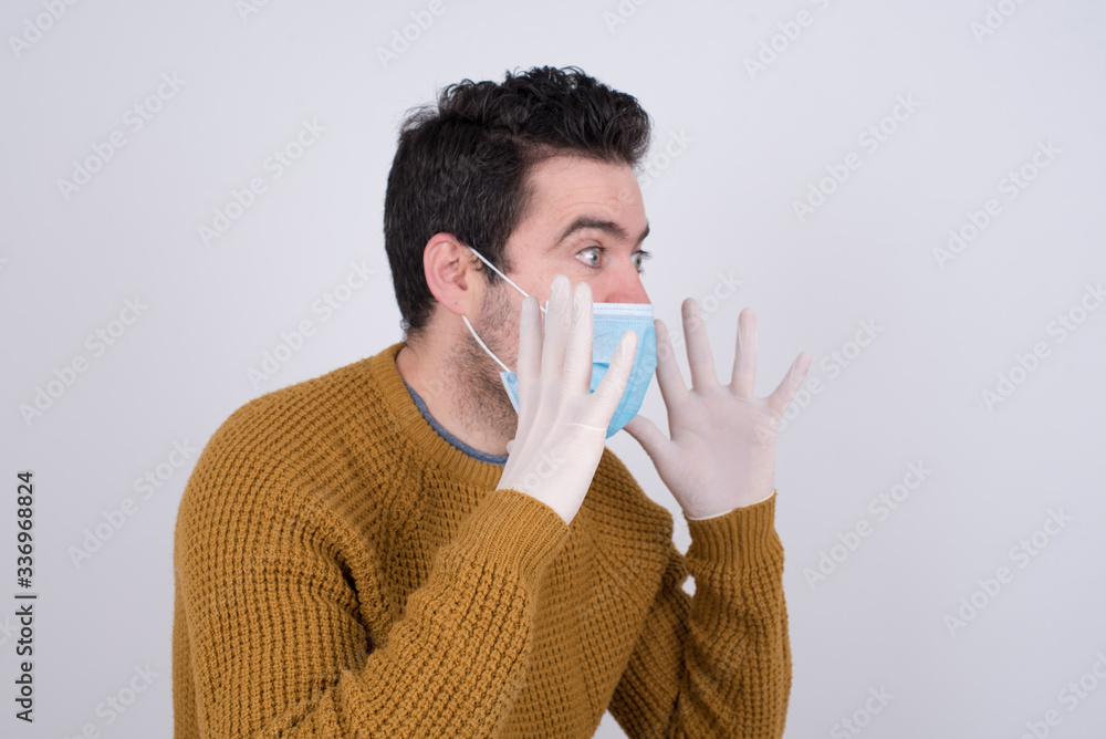 Portrait of young man with shocked facial expression, holding hands near face, screaming and looking sideways at something amazing. Stands against gray studio Wall. Portrait of young man with shocked facial expression, holding hands near face, screaming and looking sideways at something amazing. Stands against gray studio Wall.