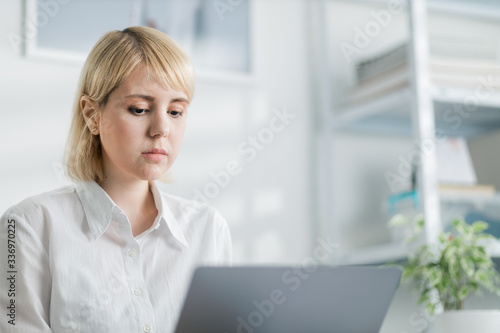 Portrait of a young woman in office working on a computer. Employee writing an e-mail in a relaxed work space. 