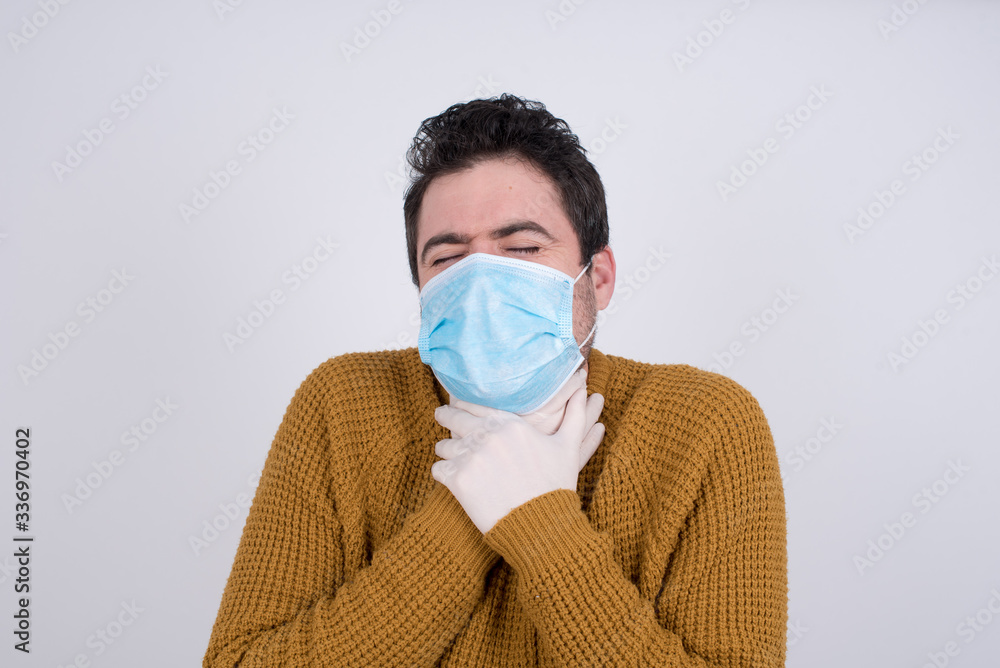 Portrait of young Caucasian man wearing medical face mask holding his throat with his hands. Protection against infectious disease coronavirus. Portrait of young Caucasian man wearing medical face mask holding his throat with his hands. Protection against infectious disease coronavirus.