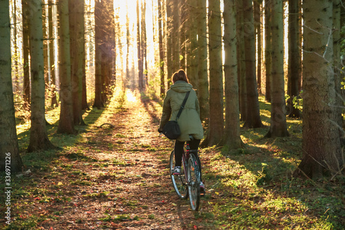 Girl rides a bicycle in a pine forest at sunset