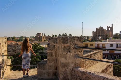 Ayia NAPA / Cyprus- 09.13.2018: a beautiful tourist girl with long unpainted hair on vacation in Cyprus stands in a full length dress and looks down at the panorama of the ancient city