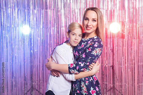 Mothers day, children and family concept - teen boy and his mom embracing on shiny party background. © satura_