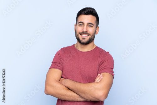 Young handsome man with beard over isolated blue background keeping the arms crossed in frontal position