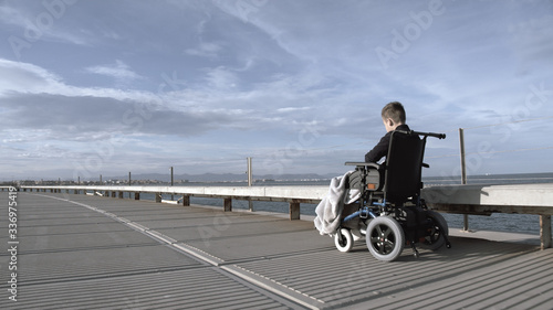 Handicapped child is lonely in this big active world. Disabled boy in wheelchair outdoor alone, shot in grey tints