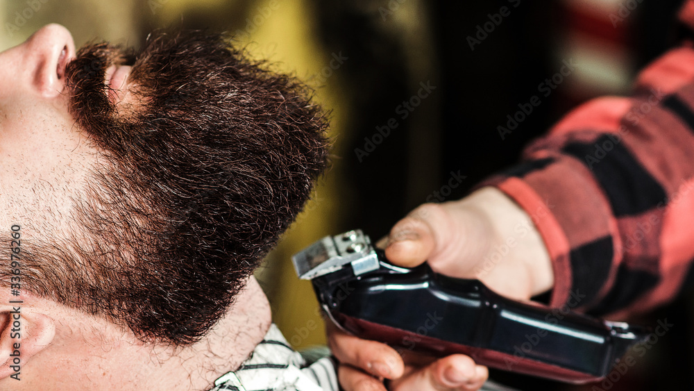 Naklejka premium Brutal bearded guy getting beard haircut by hairdresser at barbershop, close up. Getting perfect shape.