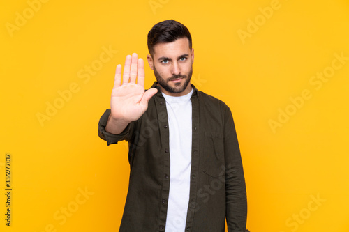 Man over isolated yellow background making stop gesture with her hand