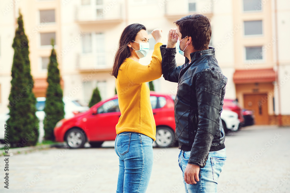 Coronavirus epidemic. Young couple greetings with elbows outdoors. Woman and man wearing face mask outdoors.