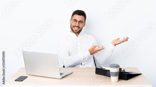 Young businessman in a workplace extending hands to the side for inviting to come