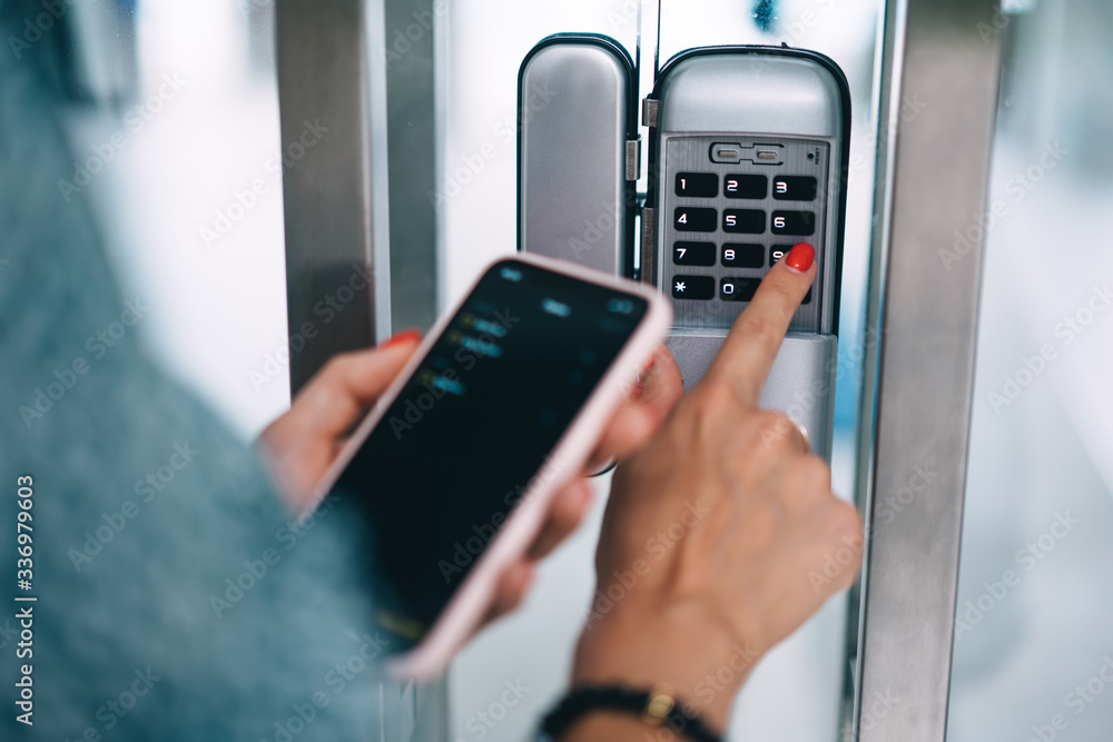 Cropped image of female entering secret key code for getting access and passing building using application on mobile phone, woman pressing buttons on control panel for disarming smart home system Cropped image of female entering secret key code for getting access and passing building using application on mobile phone, woman pressing buttons on control panel for disarming smart home system