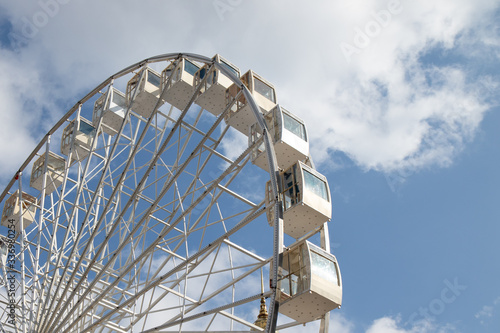 Ferris wheel in an amusement park against a on white and blue sky
