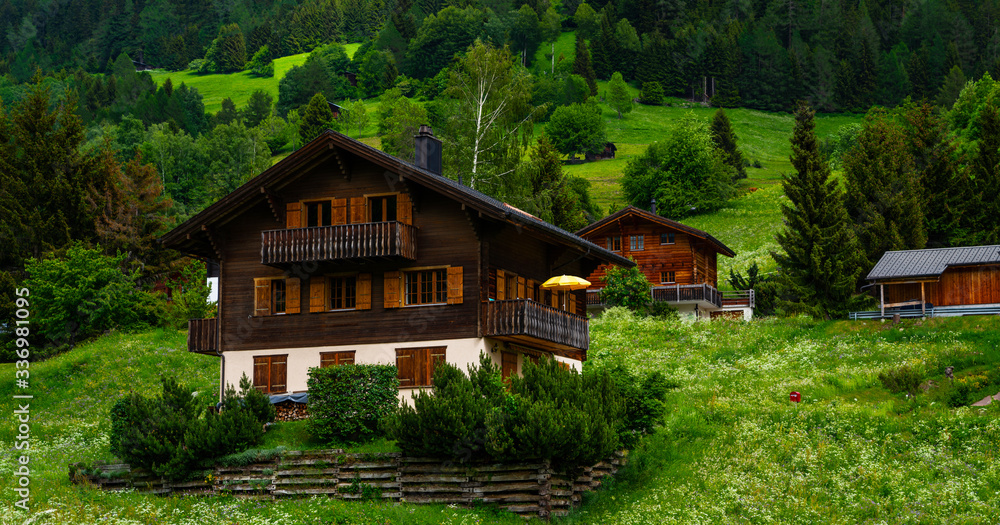 Idyllic alpine landscape scenery with traditional farmhouse and fresh green meadows, blooming flowers, and snowcapped mountain tops in spring. Idyllic alpine landscape scenery with traditional farmhouse and fresh green meadows, blooming flowers, and snowcapped mountain tops in spring.