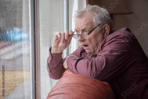 Shocked senior man looking out of window, nosy neighbor photo