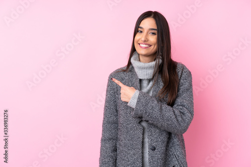 Young brunette woman over isolated pink background pointing to the side to present a product