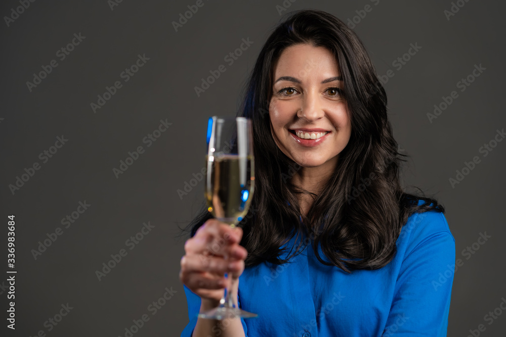 Attractive latin mature woman smiling and holding glass of champagne or wine on grey studio background. Drinking alcohol concept Attractive latin mature woman smiling and holding glass of champagne or wine on grey studio background. Drinking alcohol concept
