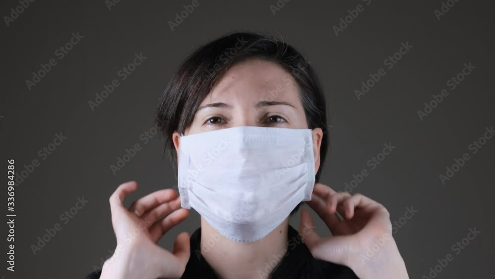 Portrait of a Caucasian woman wearing and taking off a white medical mask. Protection against contagious disease, coronavirus Portrait of a Caucasian woman wearing and taking off a white medical mask. Protection against contagious disease, coronavirus