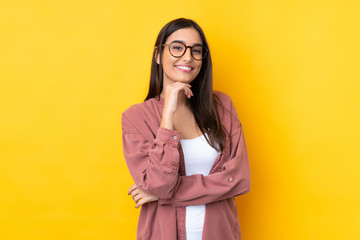 Young brunette woman over isolated yellow background with glasses and smiling