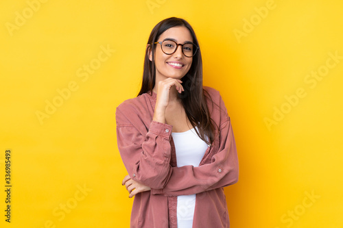 Fotobehang Young brunette woman over isolated yellow background with glasses and smiling