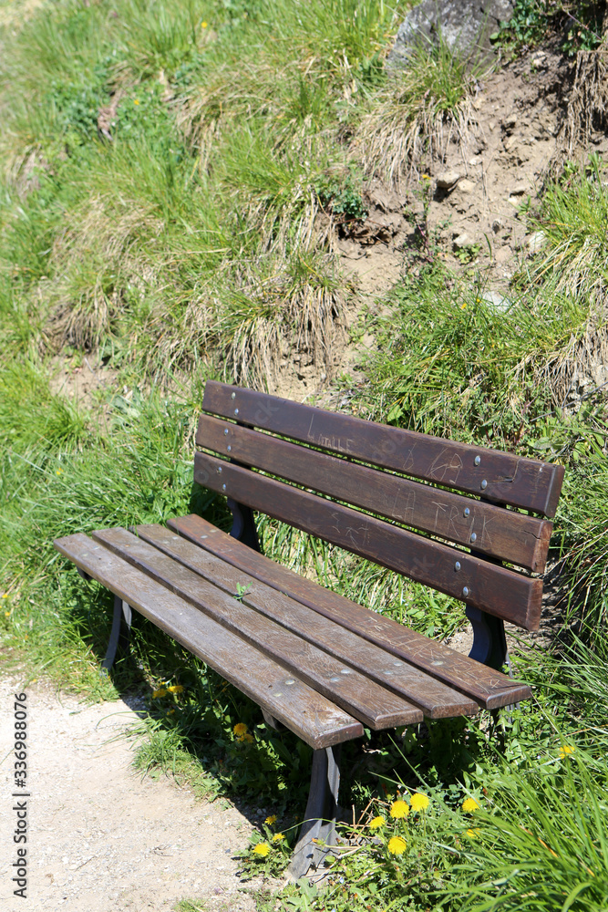Banc en bois marron sur un sentier le long d'un talus. Alpes françaises. Saint-Gervais-les-Bains. Haute-Savoie. France. Banc en bois marron sur un sentier le long d'un talus. Alpes françaises. Saint-Gervais-les-Bains. Haute-Savoie. France.