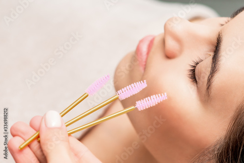 Brushes for eyelash extension in hand on background of woman face close up.