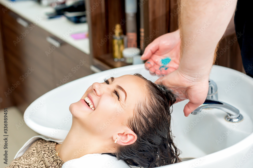 Woman laughs while close up washing hair in sink at salon.