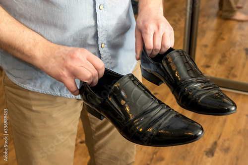 Man with classic black patent leather male shoes in hands