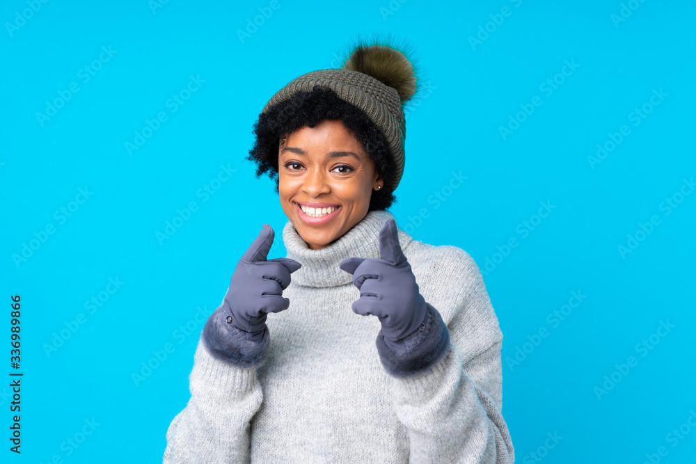 African american woman with winter hat over isolated blue background points finger at you African american woman with winter hat over isolated blue background points finger at you